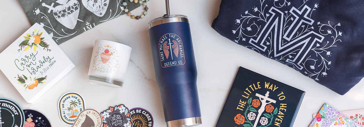 Blue tumbler with St. Michael design, decorative cards, and a pouch on a white surface